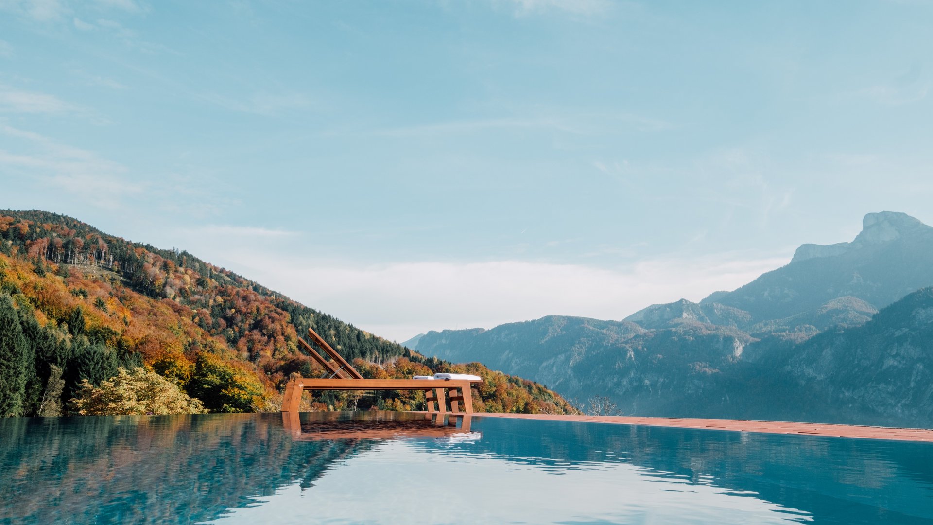 Luxuriöse Entspannung mit Bergblick Infinity Pool mit Blick auf eine bergige Landschaft und herbstliche Bäume unter blauem Himmel